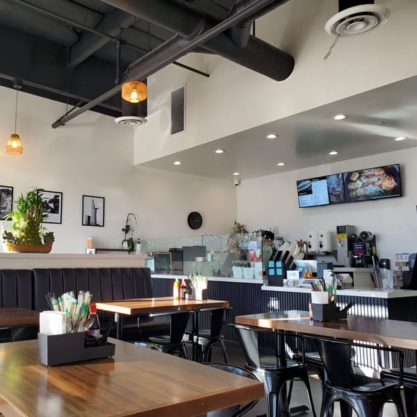 Interior of Pho Tám Cali, showing wooden tables, black booths, and a counter with menu screens.