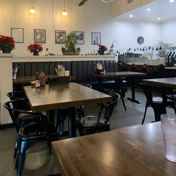 Interior of Pho Tám Cali restaurant with wooden tables, black chairs, and festive holiday decorations.