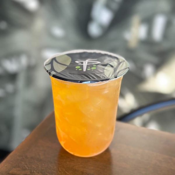 A vibrant orange drink in a clear plastic cup with a black and green branded lid.
