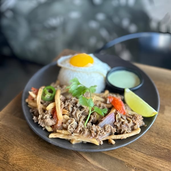Vietnamese dish with beef, fries, red peppers, onions, cilantro, rice, fried egg, and lime.