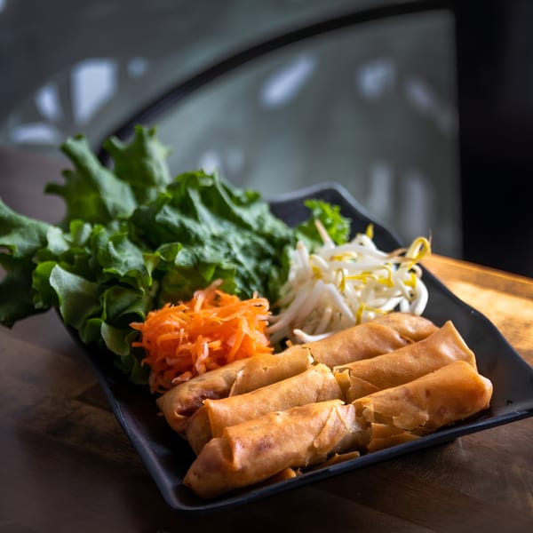 Crispy Vietnamese spring rolls with fresh lettuce, shredded carrots, and bean sprouts on a black plate.