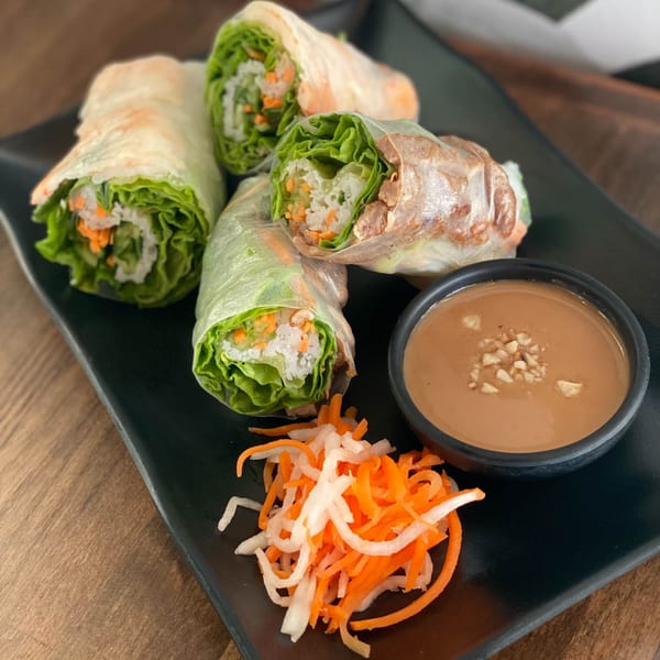 Four fresh Vietnamese spring rolls with peanut sauce and pickled carrots and daikon on a black plate.