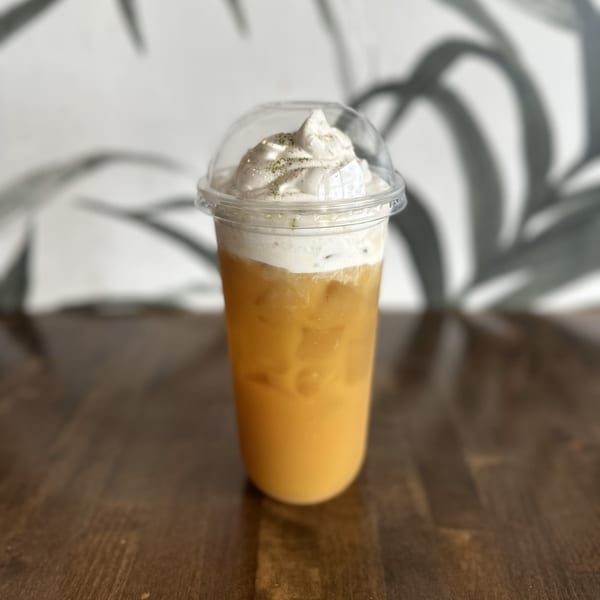 Iced Vietnamese coffee with whipped cream and a sprinkle of spice on a wooden table.