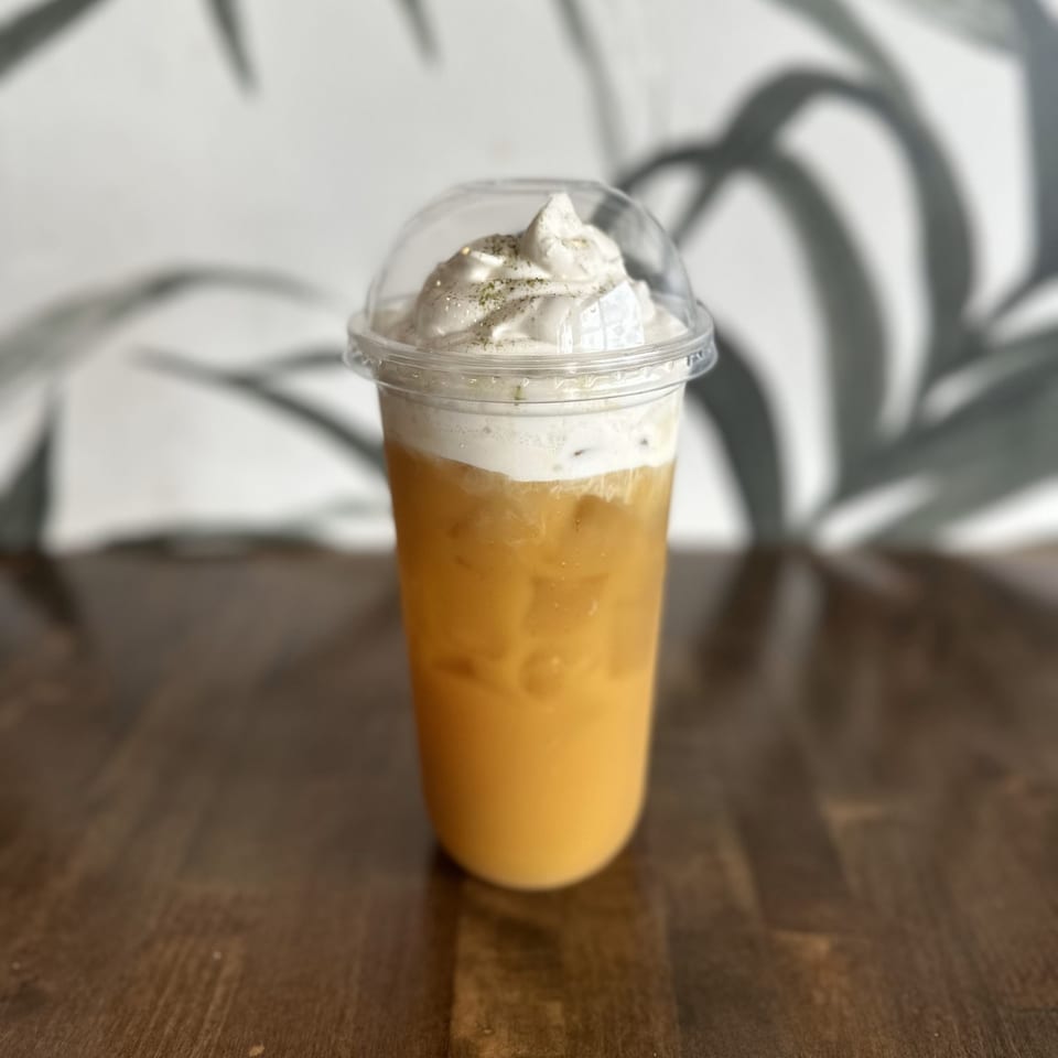 Iced Vietnamese coffee with whipped cream and a sprinkle of spice on a wooden table.