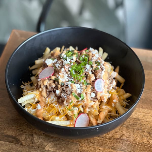 A black bowl of loaded fries topped with meat, cheese, sauce, radishes, and green onions.