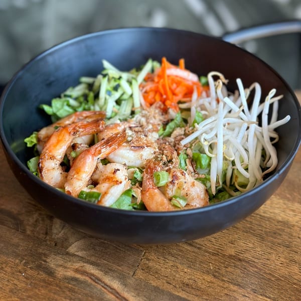 Vietnamese shrimp salad with lettuce, shredded carrots, bean sprouts, and fried shallots in a black bowl.