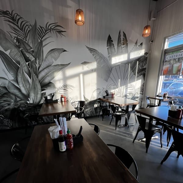 Interior of Pho Tám Cali with dark wooden tables, black chairs, and a tropical leaf mural.