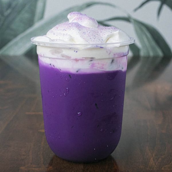A vibrant purple drink with a creamy white topping and purple sprinkles in a clear plastic cup.