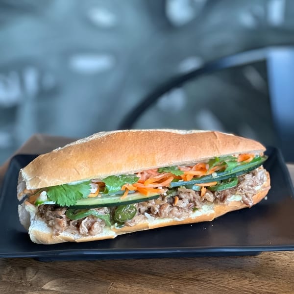 A Vietnamese banh mi sandwich with meat, cilantro, carrots, and cucumbers on a black plate.